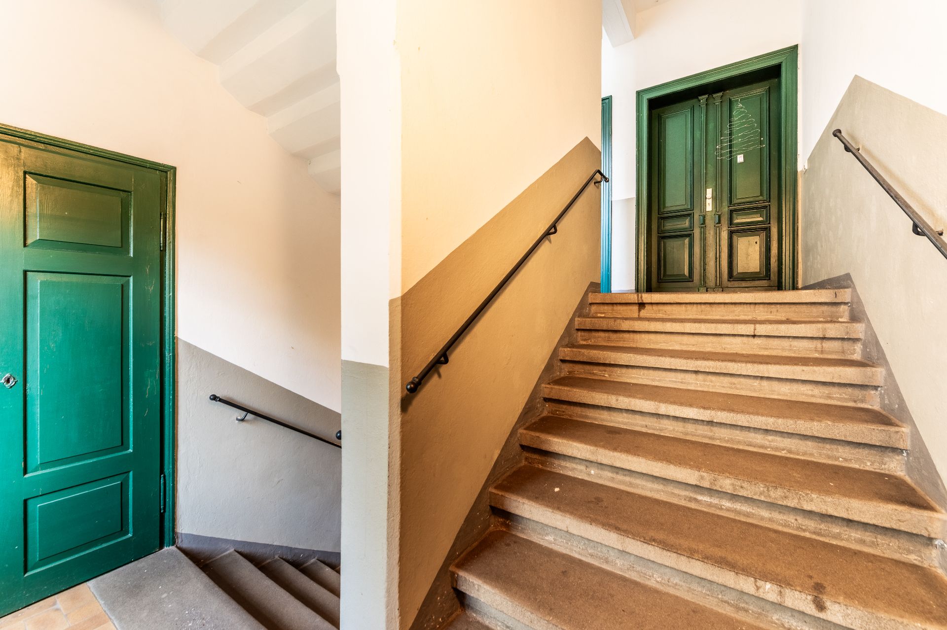 Treppenhaus mit grün gestrichenen Türen und Handläufen an den Wänden.