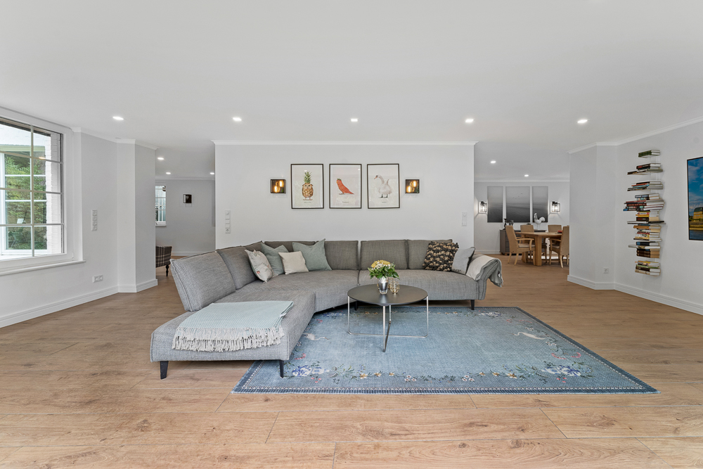 Helles Wohnzimmer mit grauem Sofa, blauem Teppich und drei Bildern an der Wand.