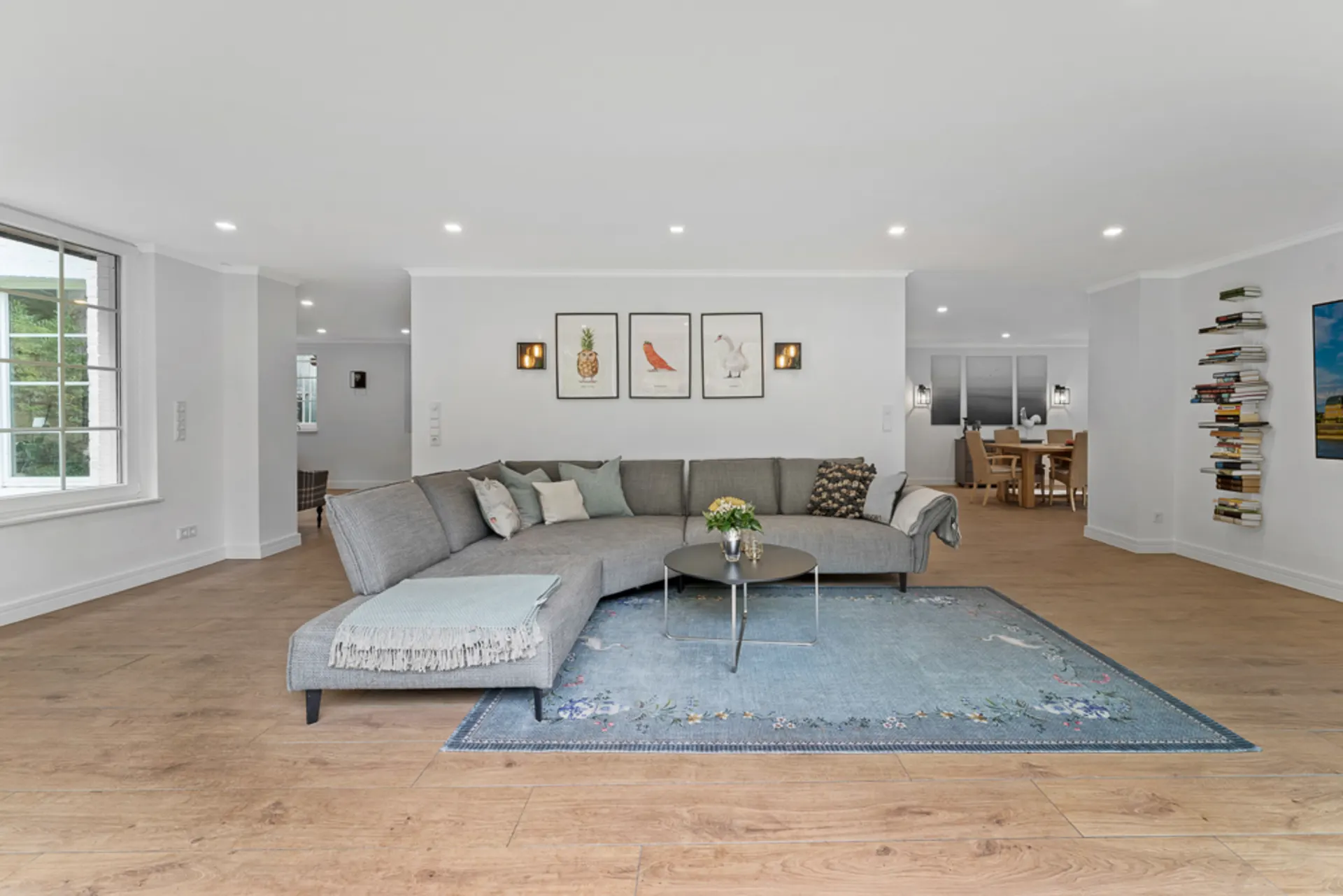 Helles Wohnzimmer mit grauem Sofa, blauem Teppich und drei Bildern an der Wand.