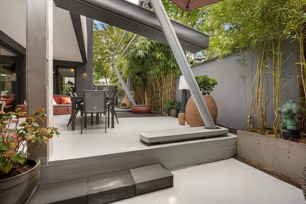 Moderne Terrasse mit Esstisch, Stühlen, Pflanzen und Markise, umgeben von Bambus und Wänden.