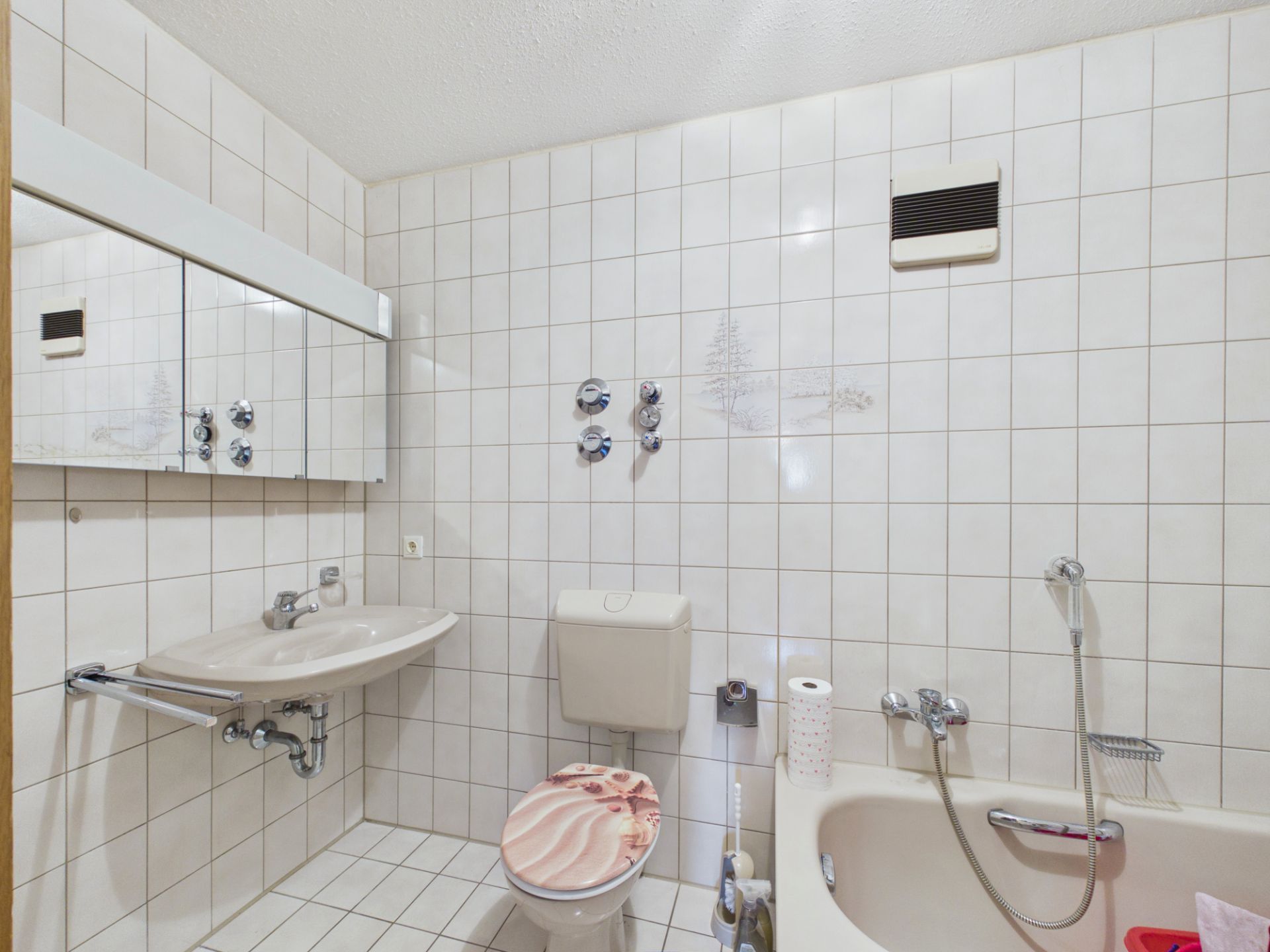 Helles Badezimmer mit Waschbecken, Toilette, Badewanne und weiß gefliesten Wänden.