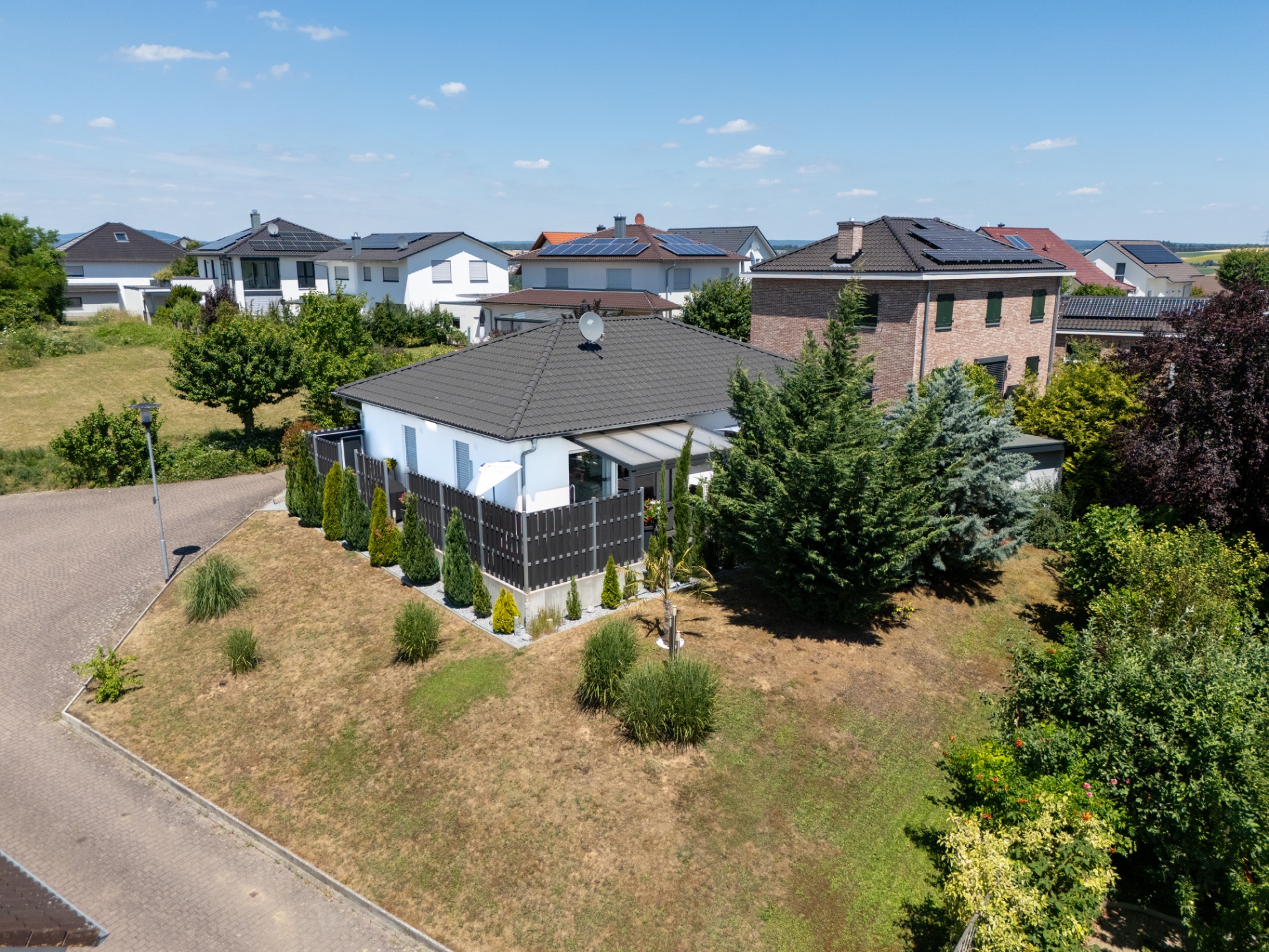 Einfamilienhaus mit Garten und Terrasse an einer Straßenecke in einem Wohngebiet.