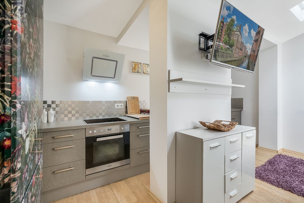 Moderne Küche mit Herd und Ofen, daneben eine weiße Kommode und ein Fernseher an der Wand.