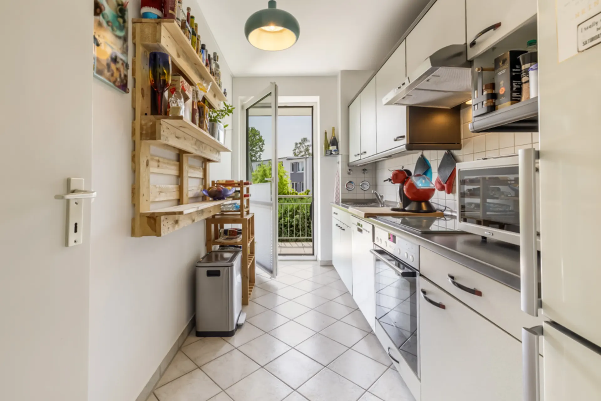 Helle, schmale Küche mit weißen Schränken, Regalen und Glastür zum Balkon.