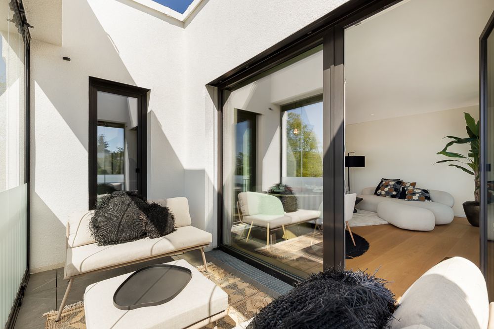 Helle Terrasse mit Sitzgelegenheiten und Zugang zu modernem Wohnzimmer mit weißen Möbeln.
