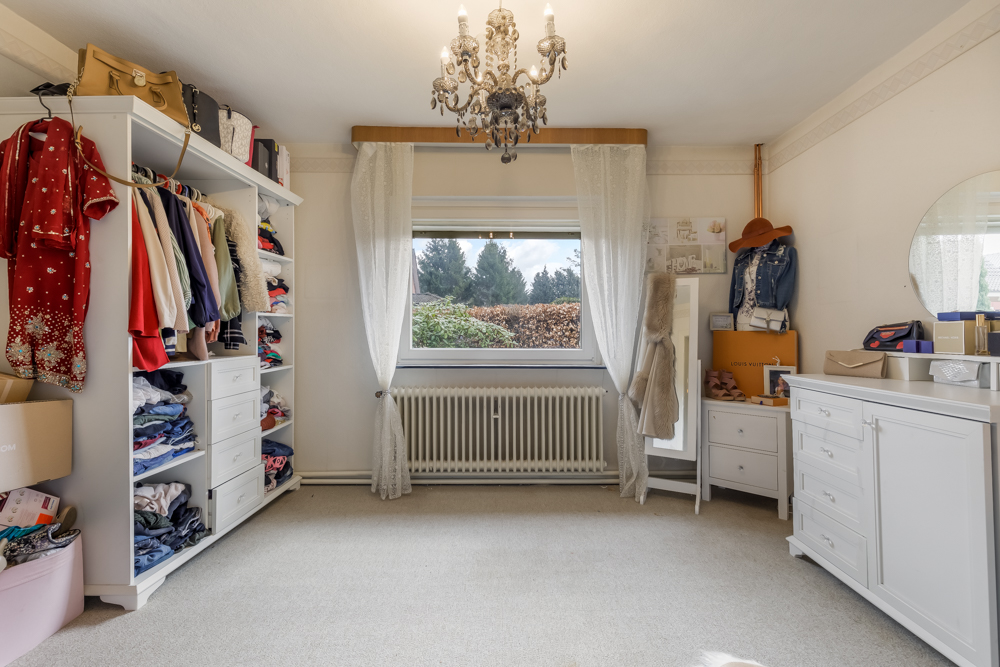 Helles Ankleidezimmer mit Kleiderschrank, Kommode, Spiegel und Fenster mit Blick ins Grüne.