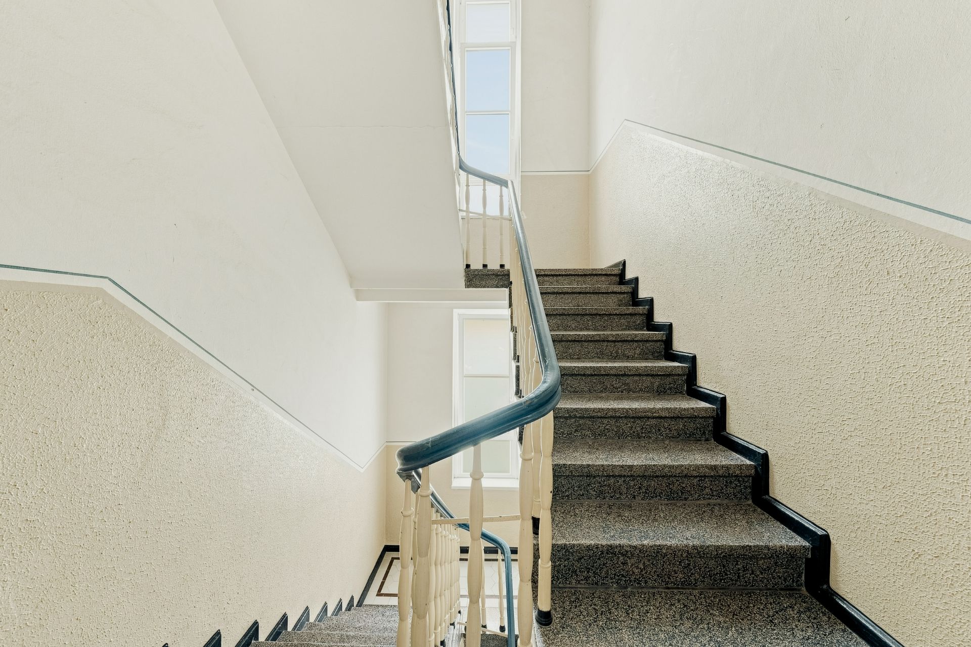Helles Treppenhaus mit Geländer und großen Fenstern in einem Wohngebäude.