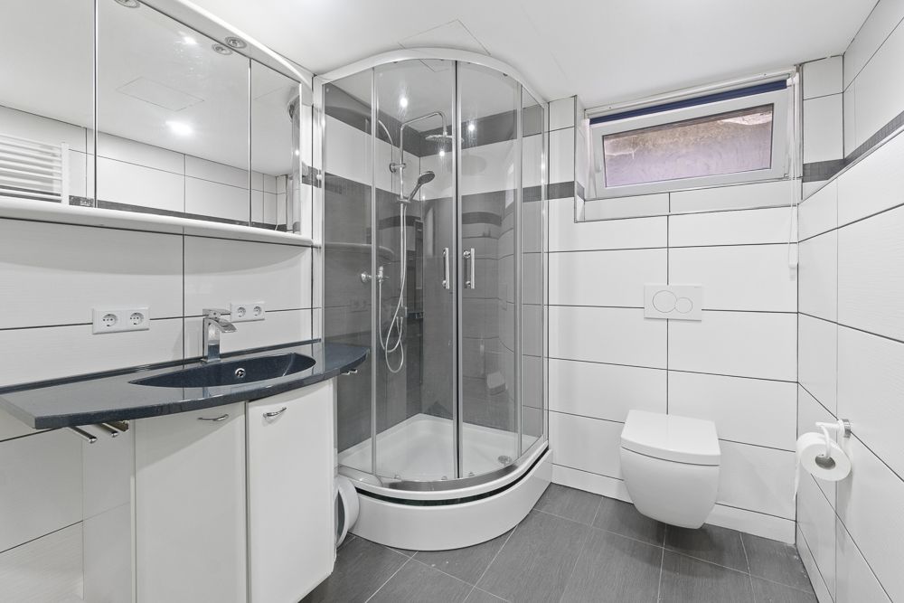 Modernes Badezimmer mit Eckdusche, Waschtisch mit Spiegel und Wandtoilette.