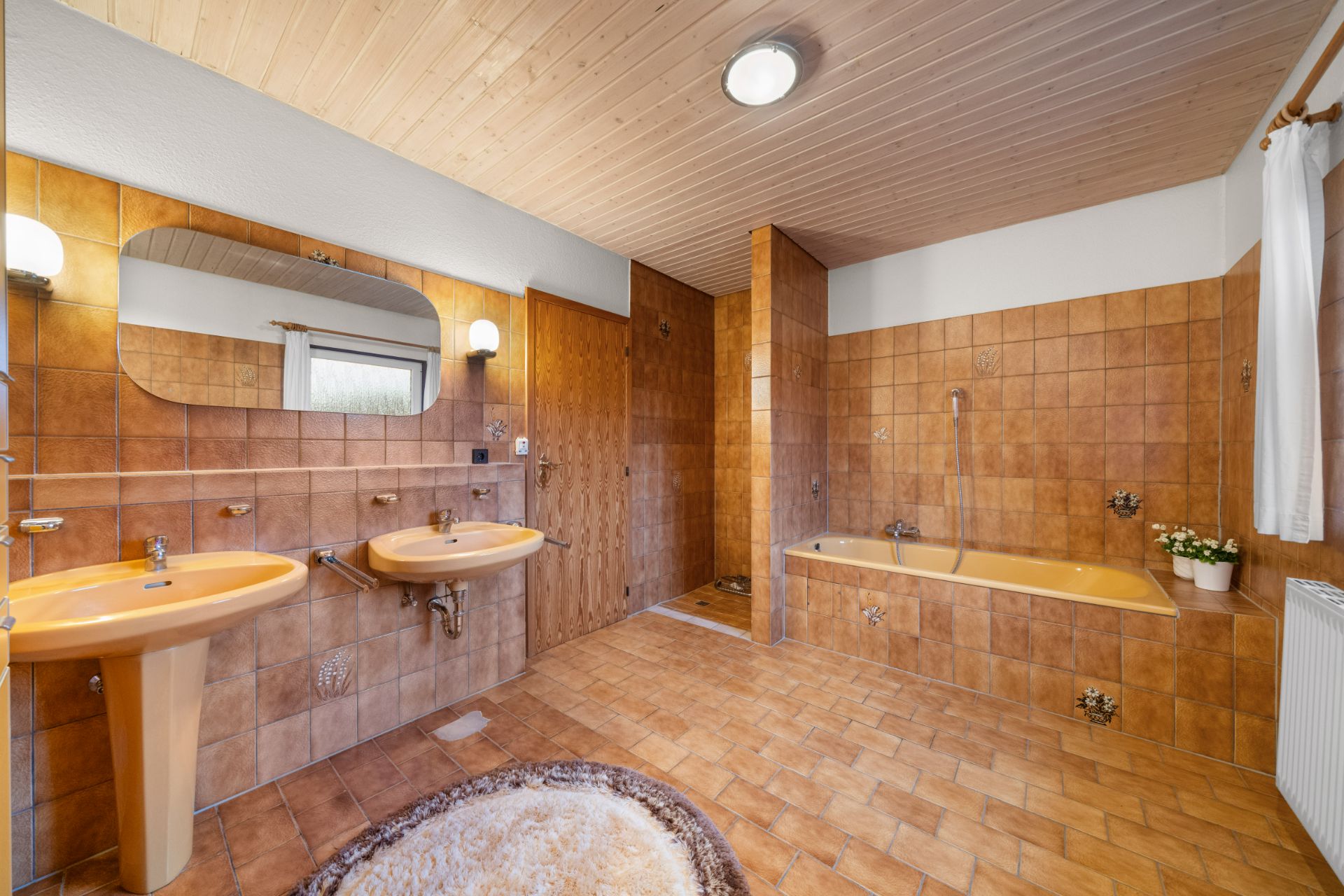 Großes Badezimmer mit zwei Waschbecken, Badewanne, Dusche und hellbraunen Fliesen.