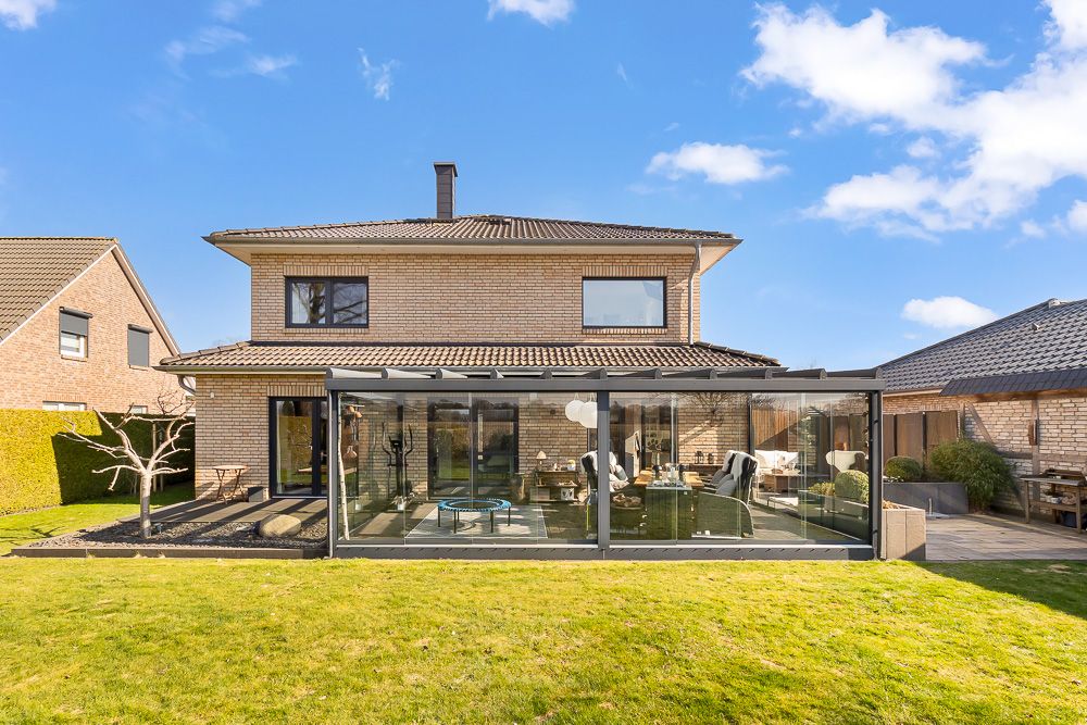 Zweistöckiges Haus mit Wintergarten und gepflegtem Rasen im Vordergrund.