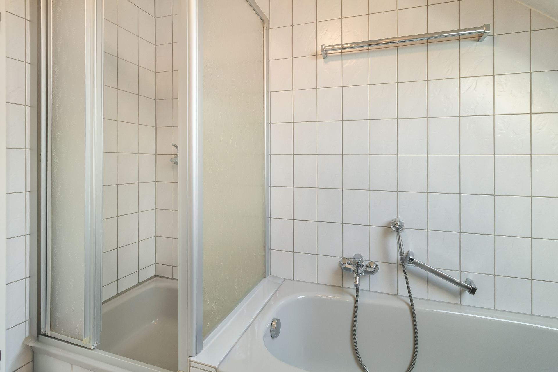 Badezimmer mit Badewanne, Duschabtrennung und weißen Fliesen.