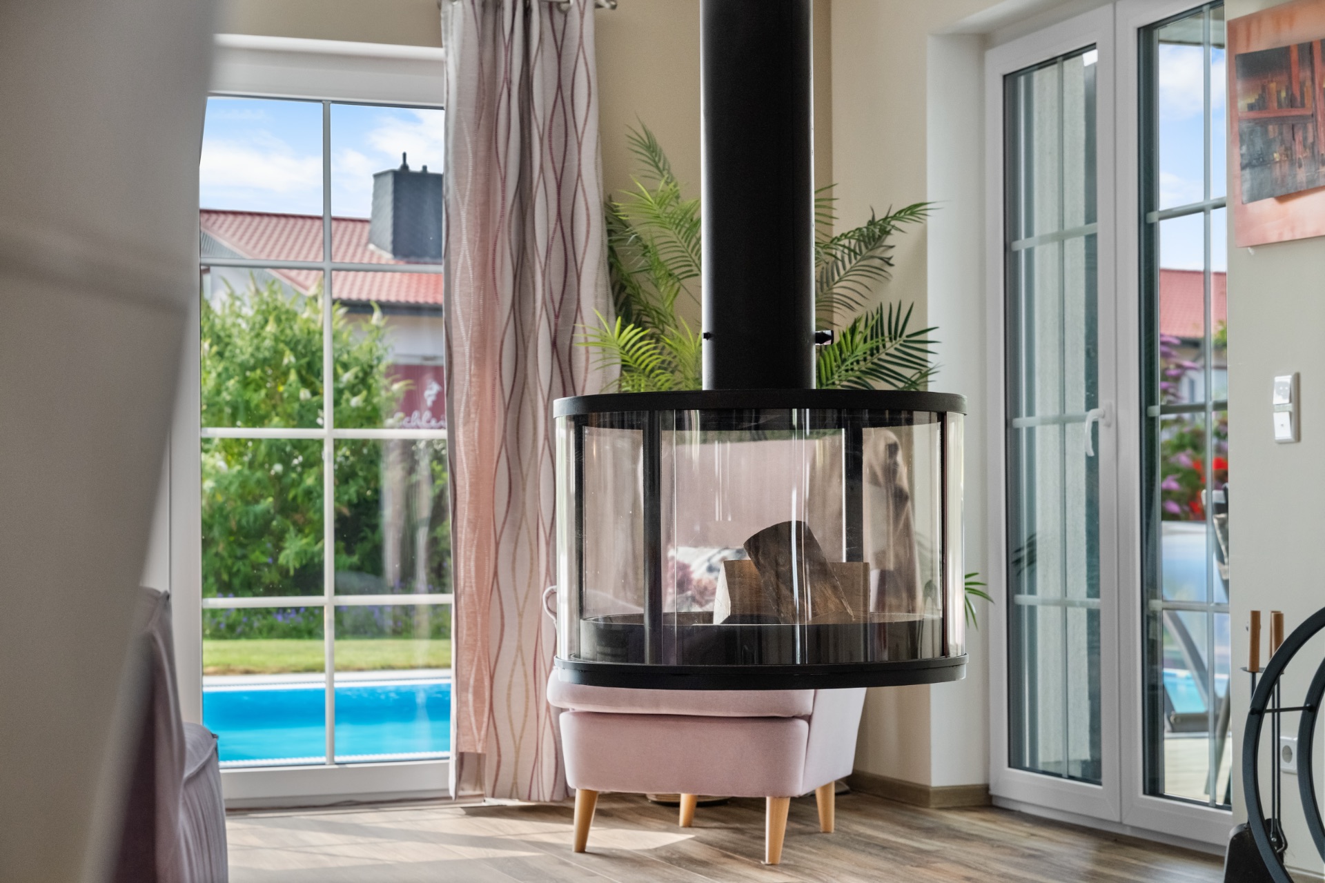 Modernes Wohnzimmer mit Kamin, großen Fenstern und Blick auf einen Garten mit Pool.