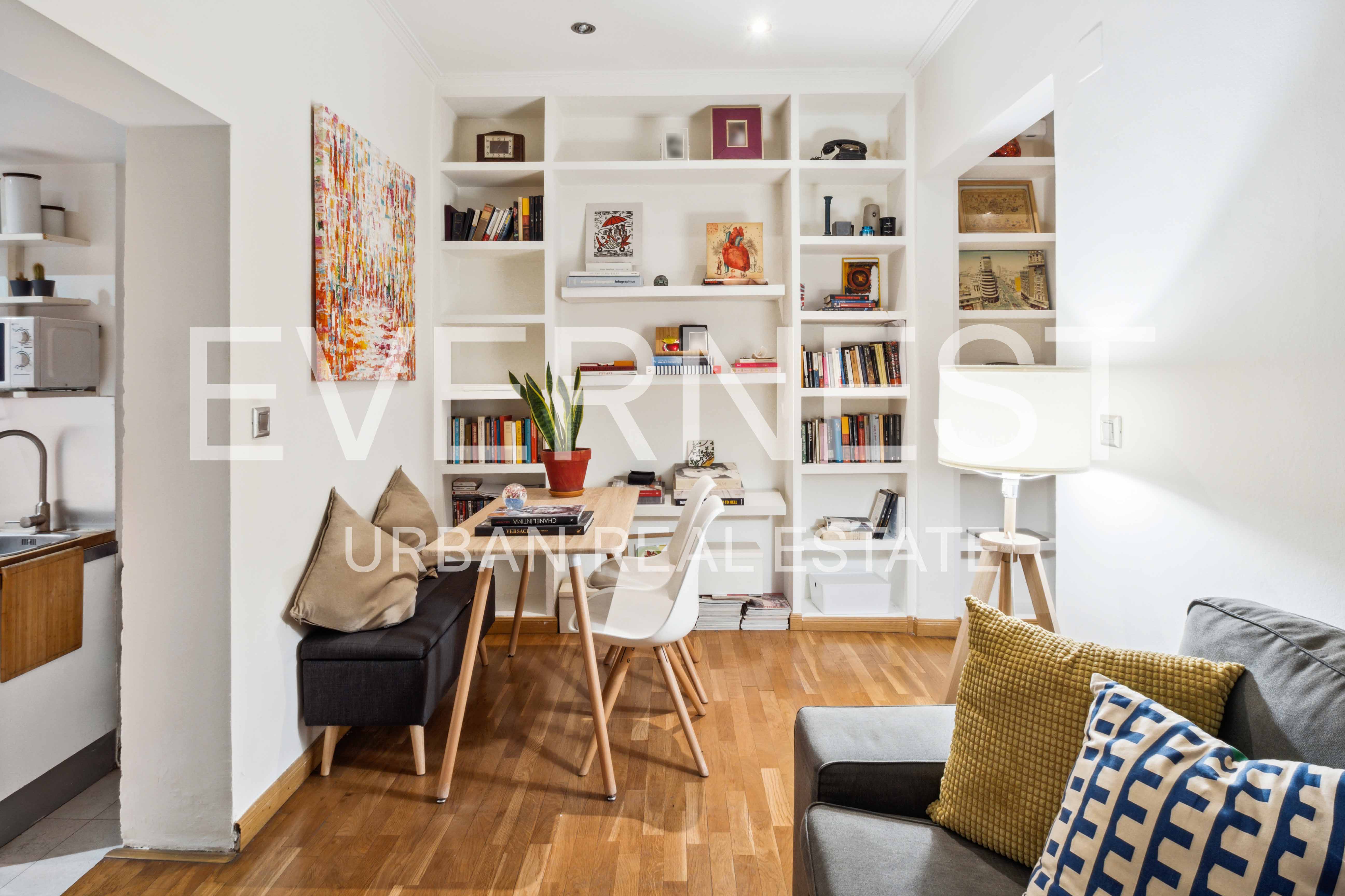 Wohnzimmer mit Bücherregal, Esstisch, Stuhl, Sofa und bunter Wandkunst.