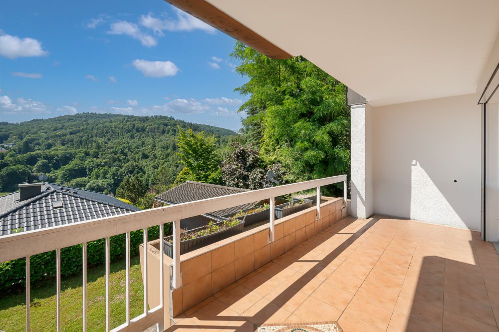 Großer Balkon mit Fliesenboden und Blick auf grüne Hügel und Bäume.