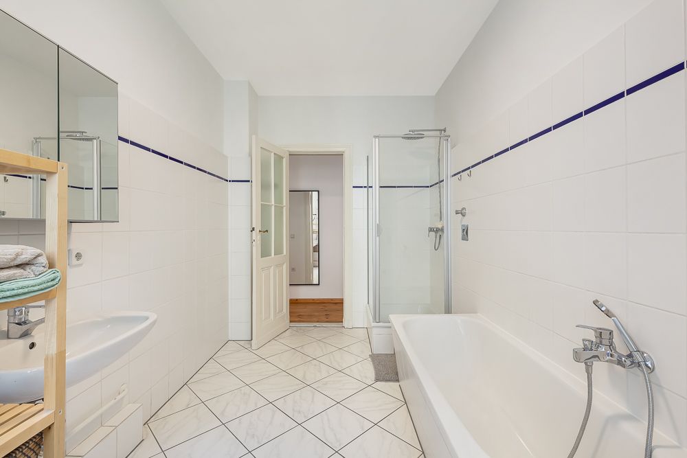 Helles Badezimmer mit Badewanne, Dusche, Waschbecken und Regal mit Handtüchern.