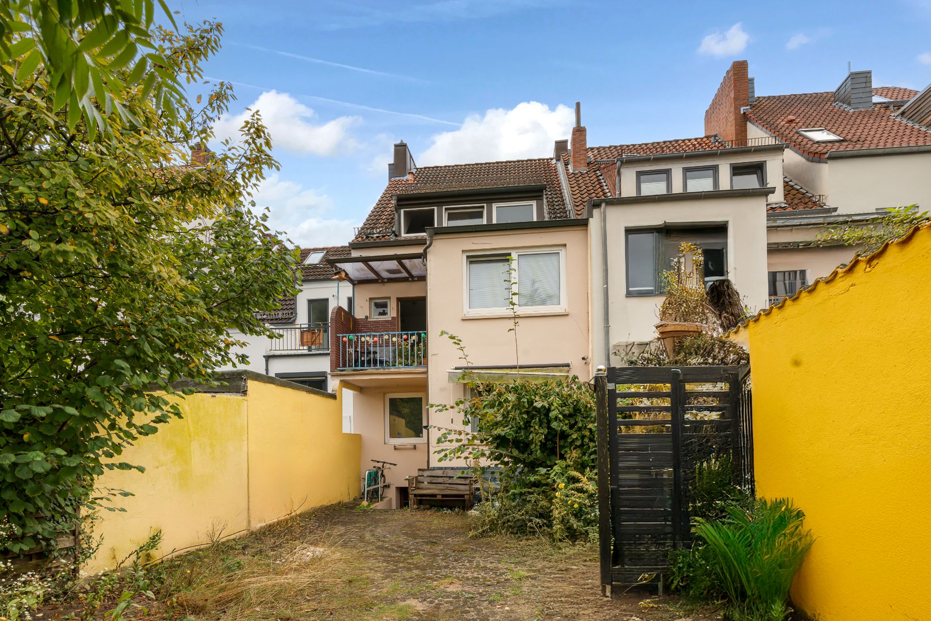 Hinterhof eines Wohnhauses mit gelber Wand, Pflanzen und Terrasse.