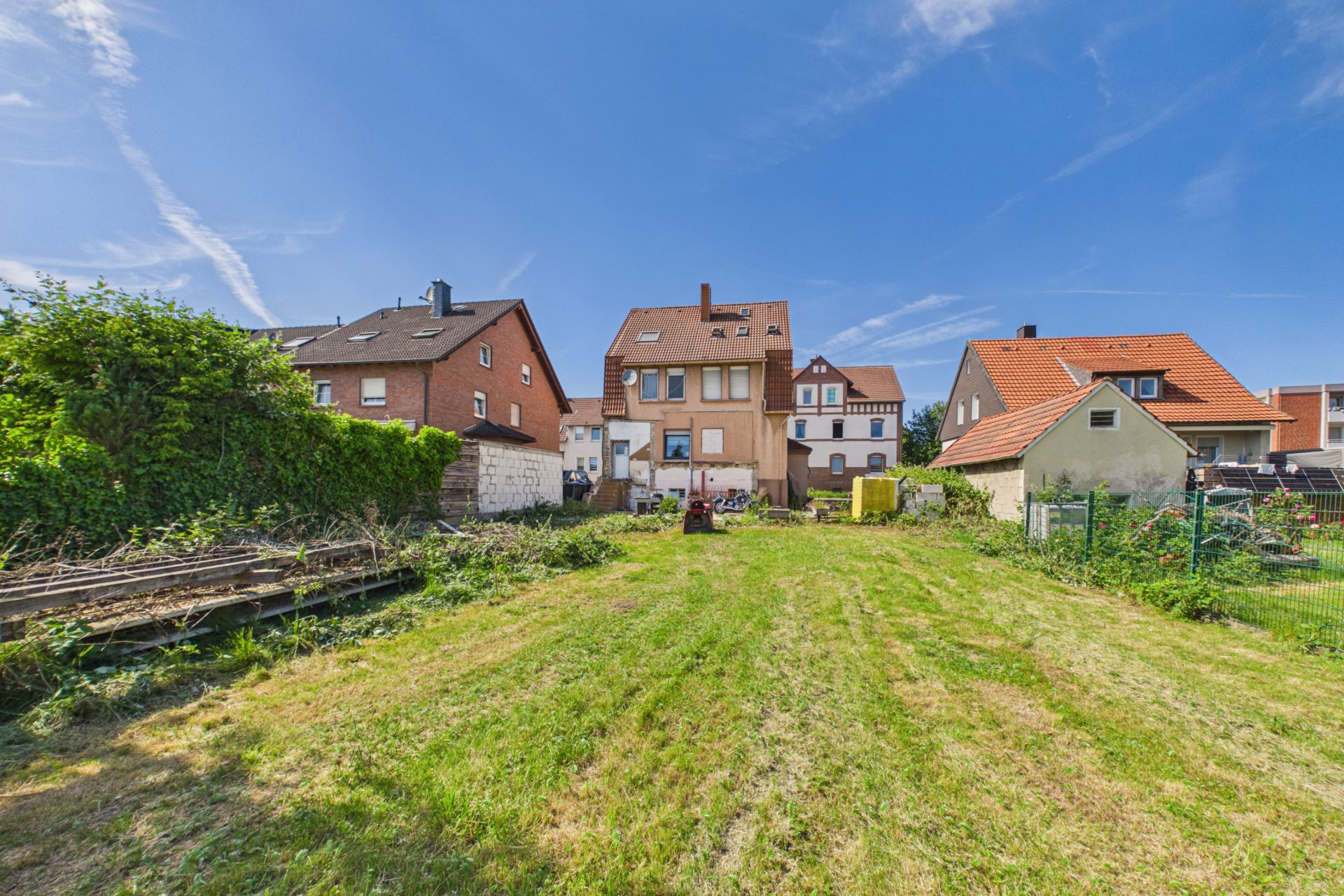 Großer, gepflegter Garten mit Blick auf mehrere Wohnhäuser bei sonnigem Himmel.