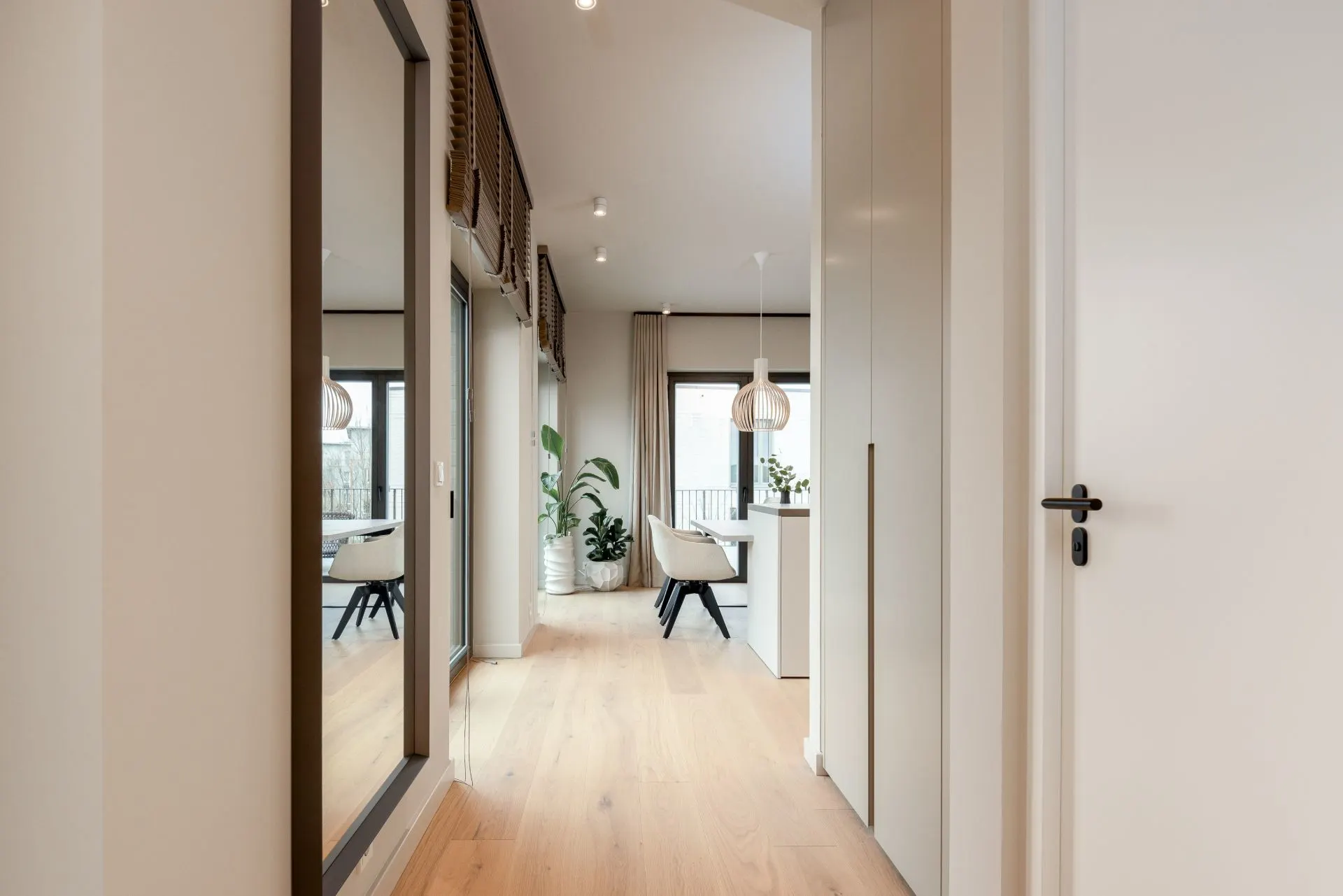 Heller Flur mit Holzfußboden, großem Spiegel, Pflanzen und Blick ins Esszimmer.