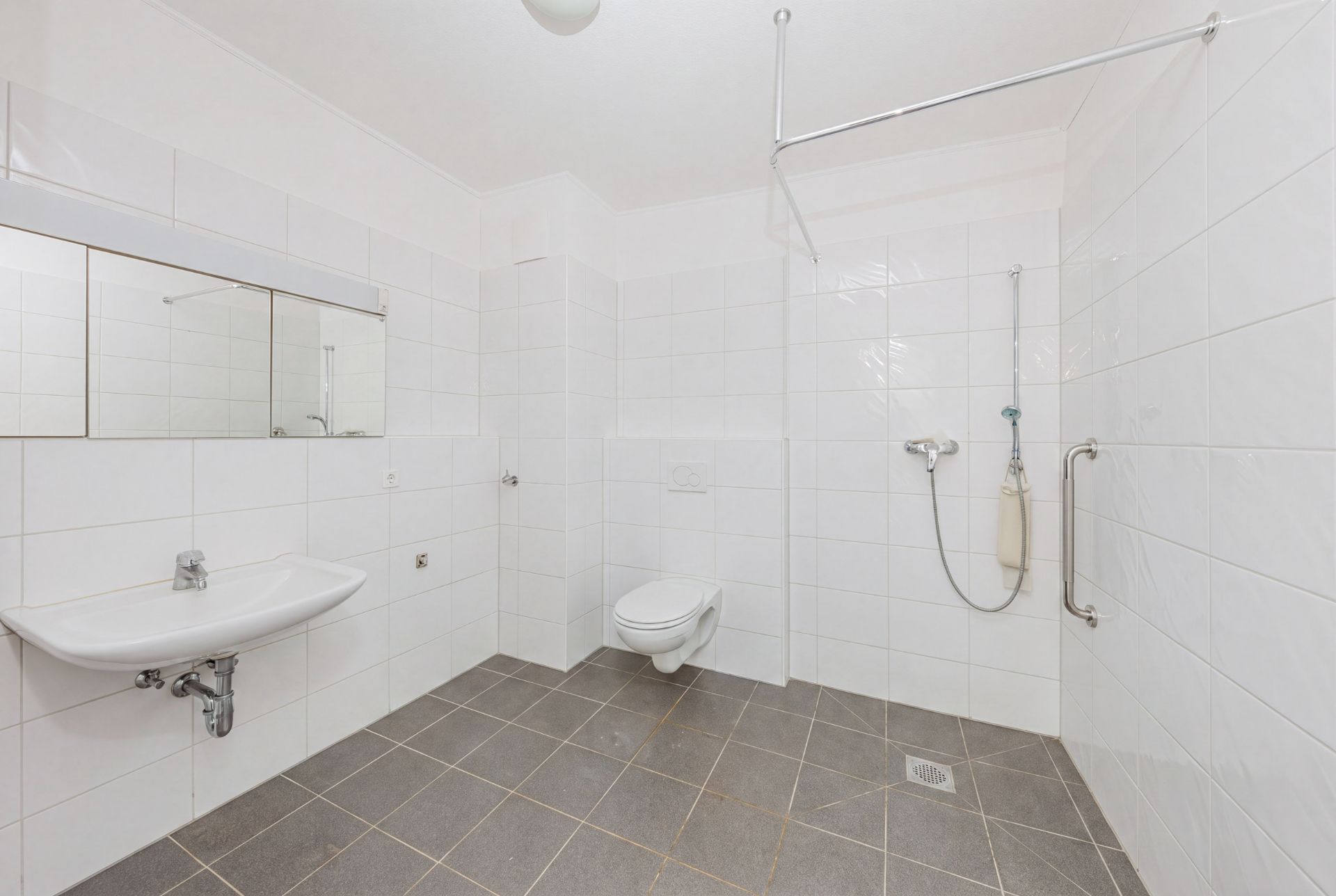 Barrierefreies Bad mit Wandspiegel, Waschbecken, WC und ebenerdiger Dusche.