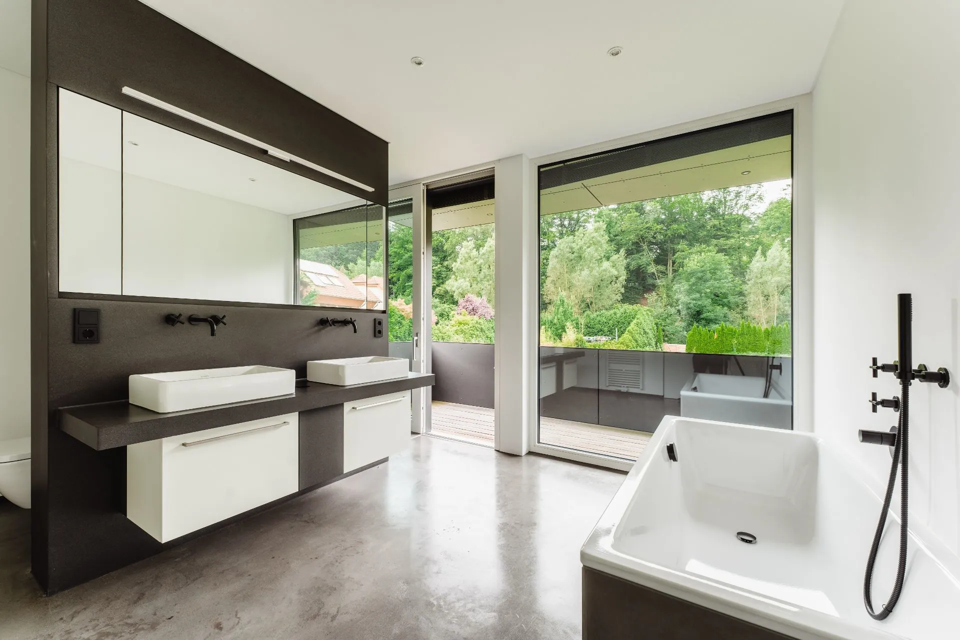 Modernes Badezimmer mit zwei Waschbecken, Badewanne und großen Fenstern mit Blick ins Grüne.
