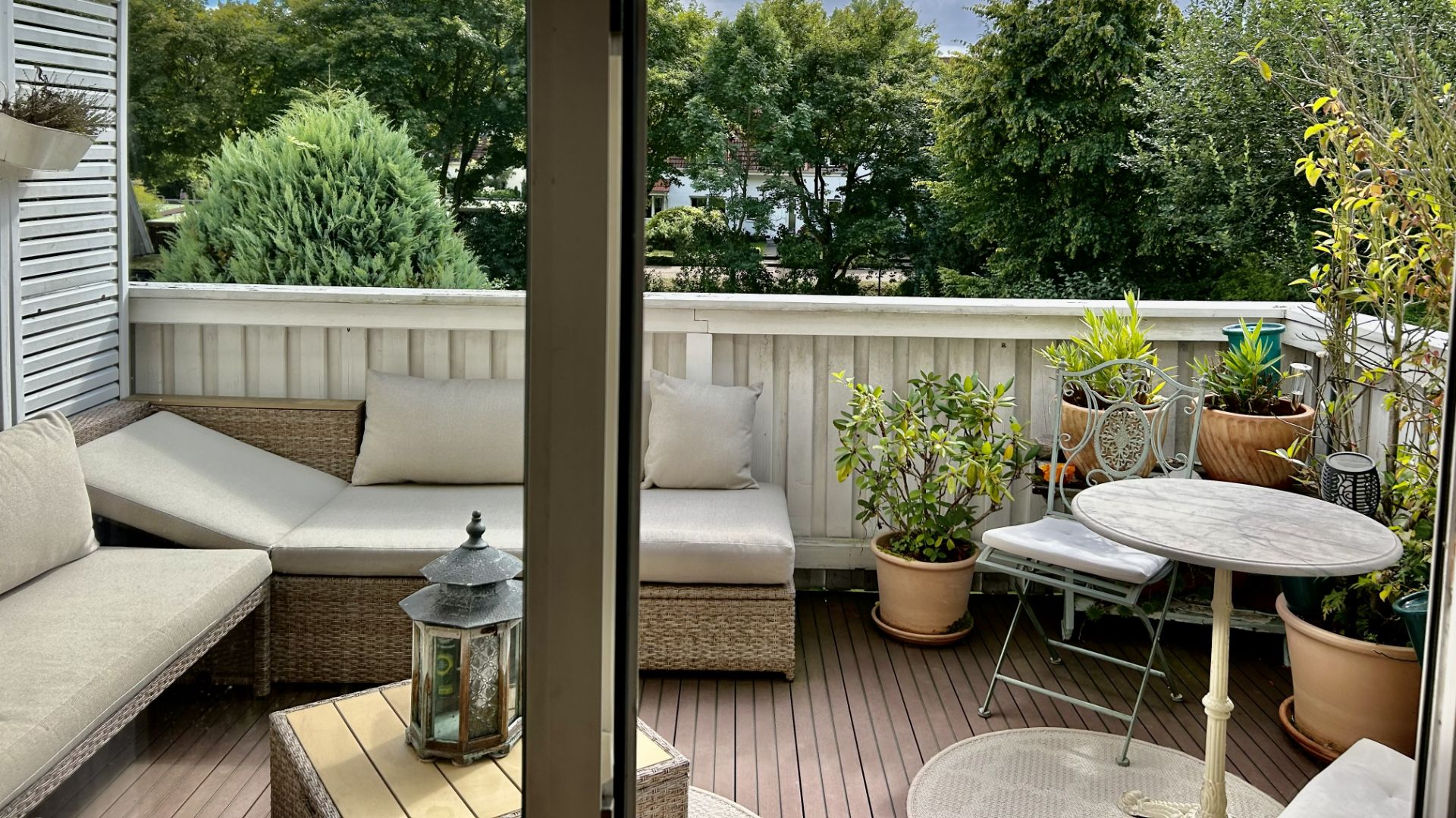Balkon mit Sitzbank, kleinem Tisch, Stühlen und vielen Pflanzen in Töpfen, Blick ins Grüne.