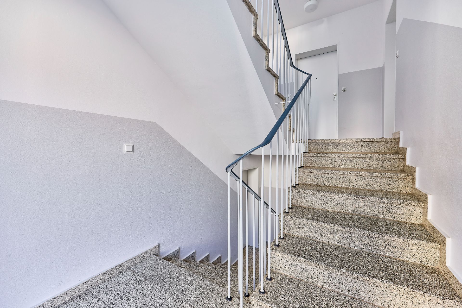Innen-Treppenhaus mit Stufen, Geländer und einer geschlossenen Tür im Obergeschoss.