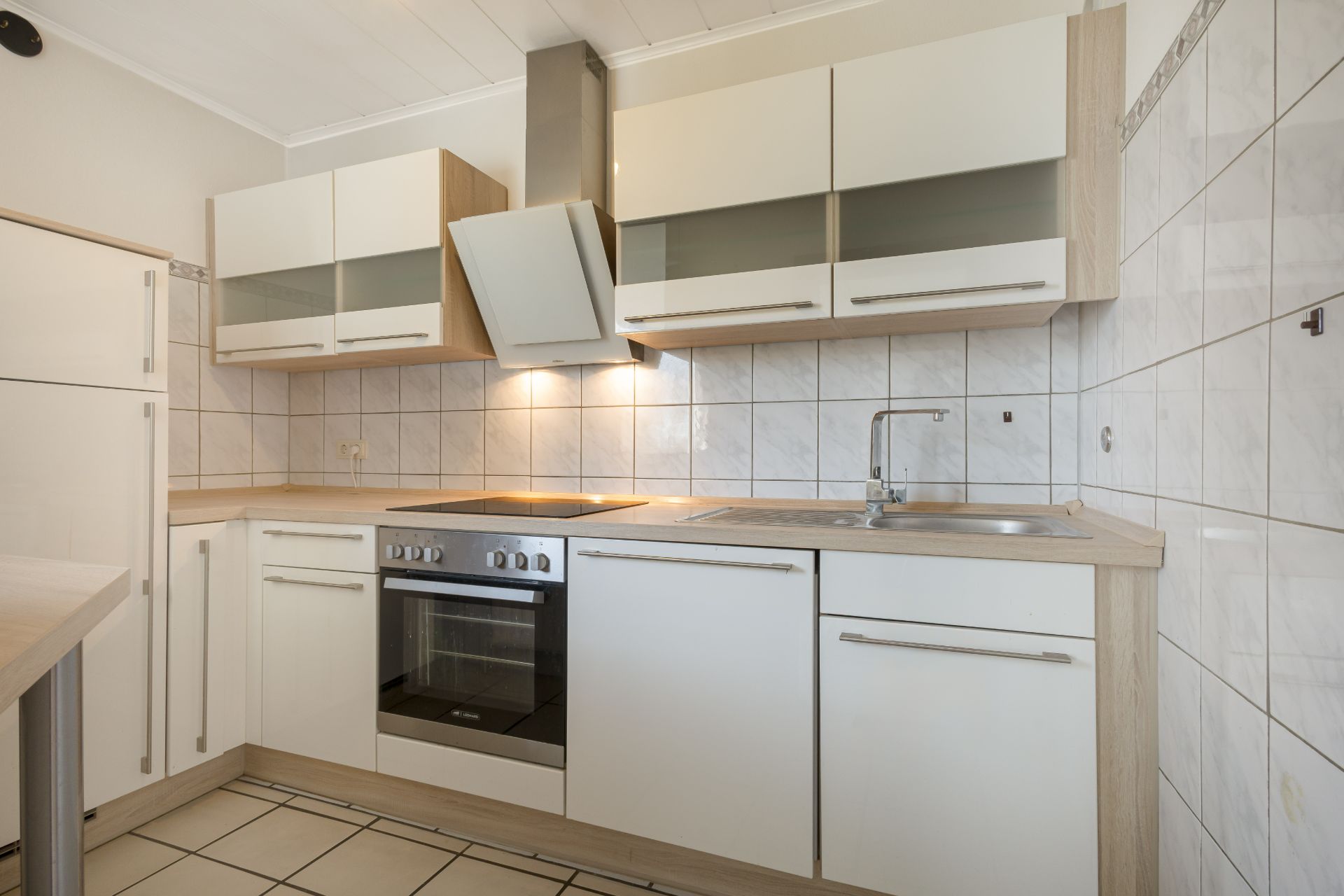 Moderne Einbauküche mit Herd, Backofen, Spüle und weißen Schränken, Wandfliesen im Hintergrund.
