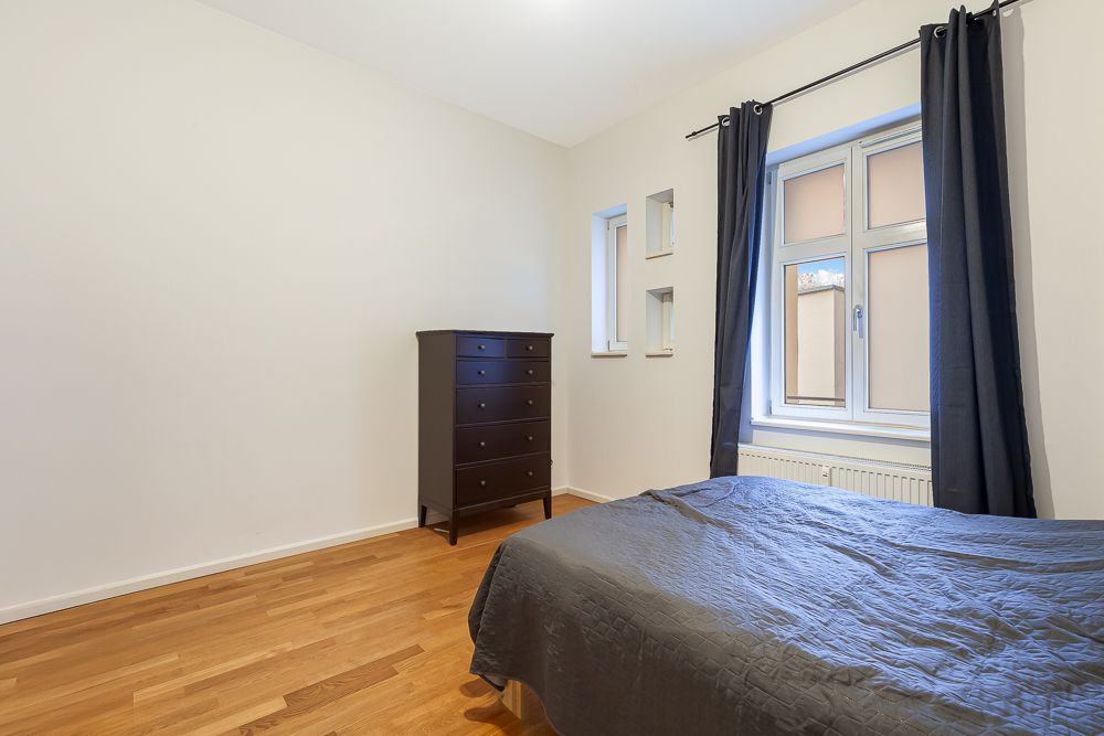 Schlafzimmer mit Holzfußboden, einem Bett, Kommode, Fenster und dunklen Vorhängen.