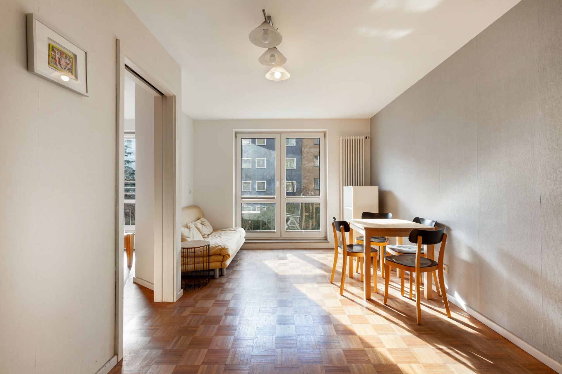 Helles Wohnzimmer mit Esstisch, vier Stühlen, Sofa und großen Fenstern.