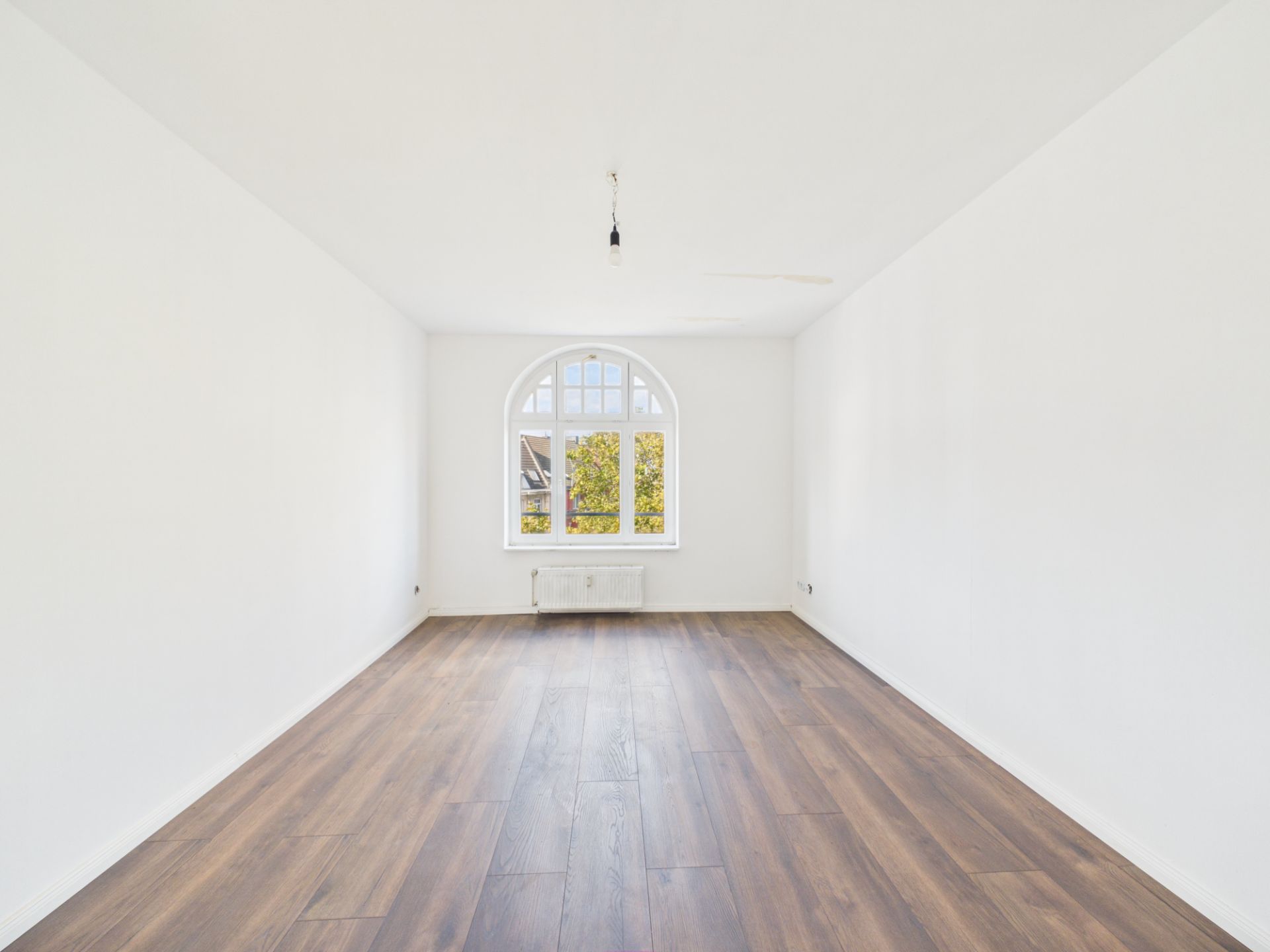 Heller, leerer Raum mit weißem Wänden, Holzfußboden und großem Rundbogenfenster.