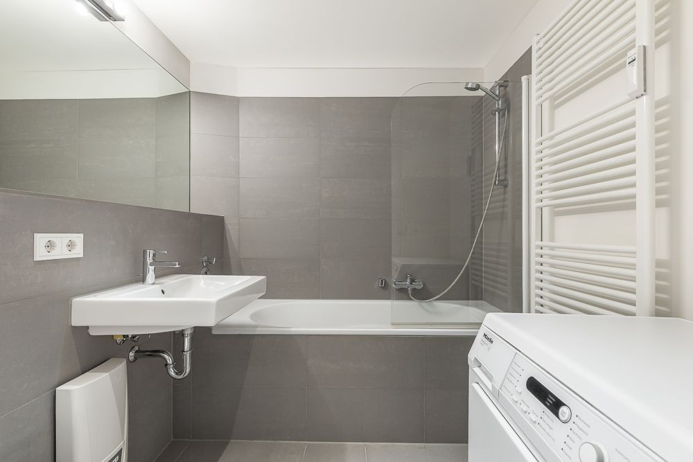 Modernes Badezimmer mit Badewanne, Waschbecken, Waschmaschine und Handtuchheizkörper.