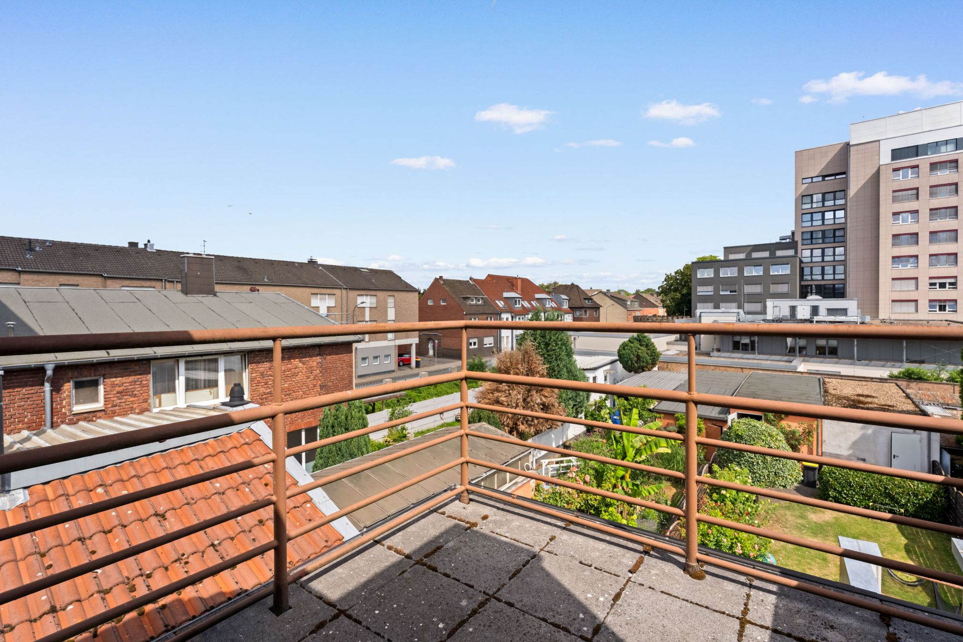 Blick von einem Balkon einer Wohnung auf Nachbarhäuser und einen Garten.