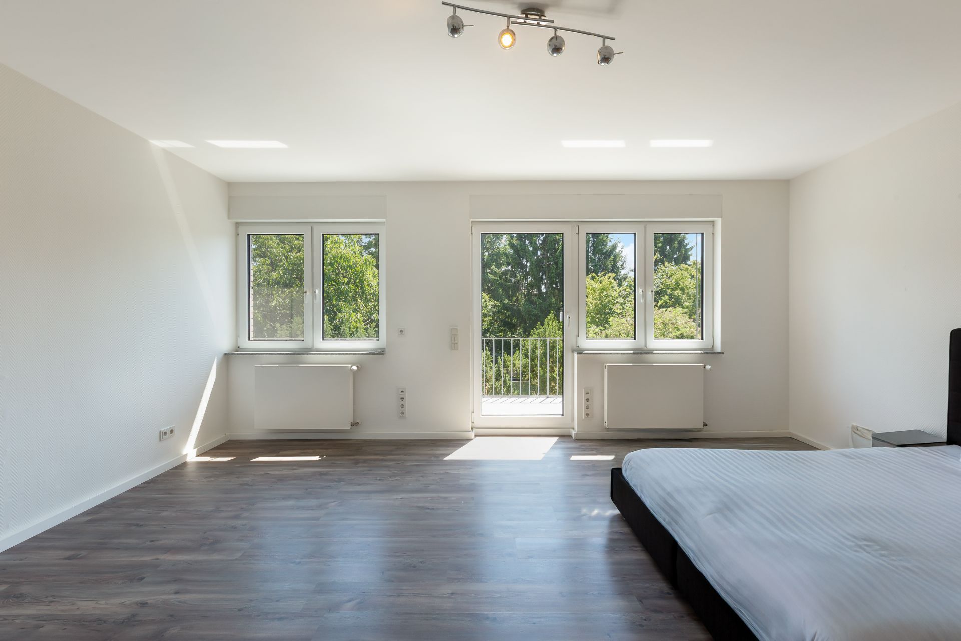 Helles Schlafzimmer mit großen Fenstern, Balkontür und Bett auf der rechten Seite.