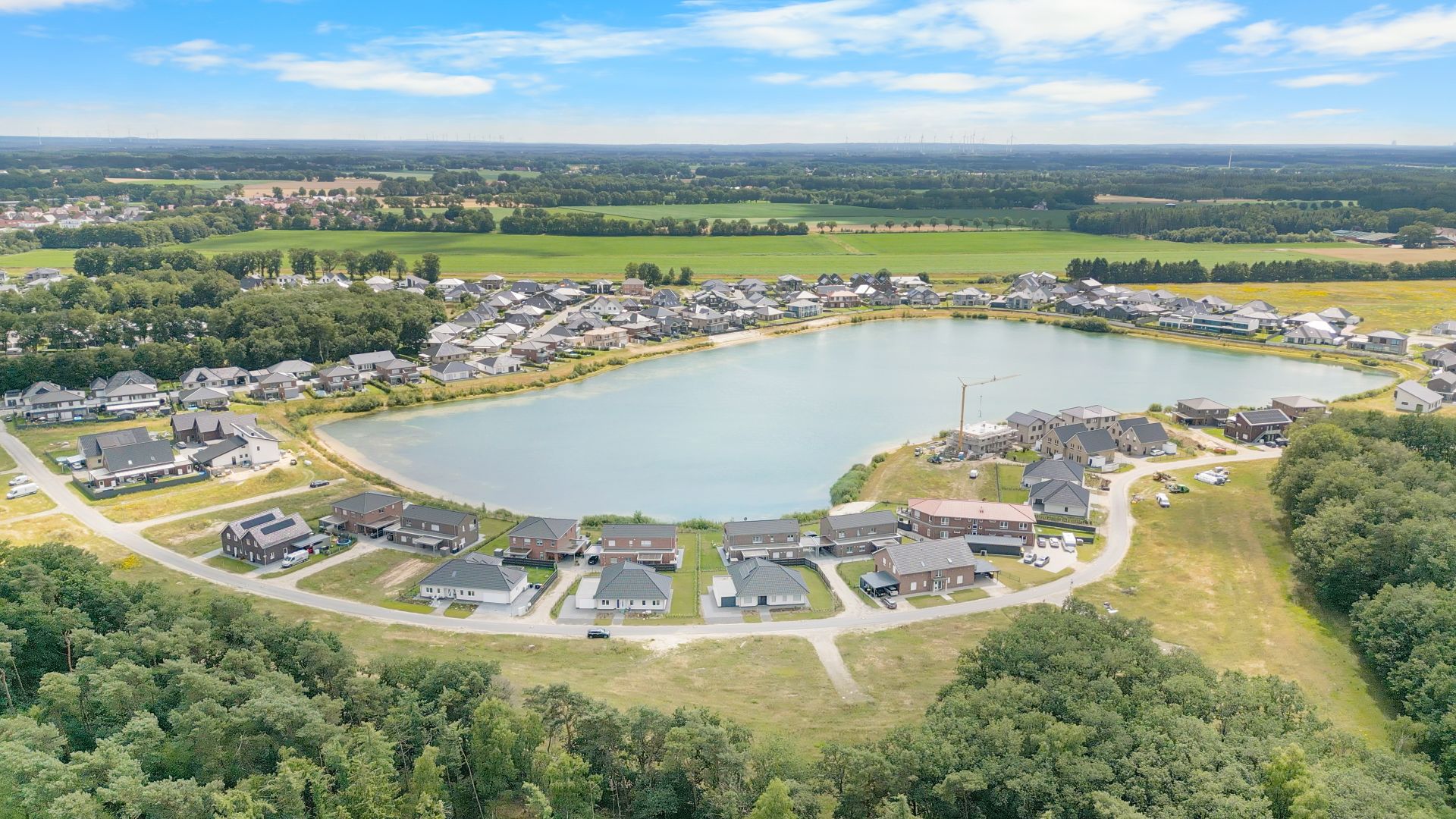 Wohnsiedlung mit Häusern rund um einen großen See und umgeben von Wald und Feldern.