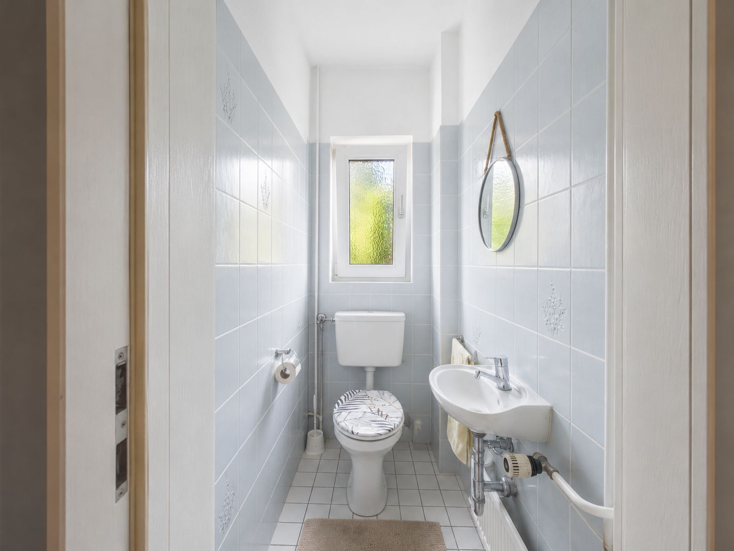 Kleines Badezimmer mit Toilette, Waschbecken, Spiegel und Fenster.