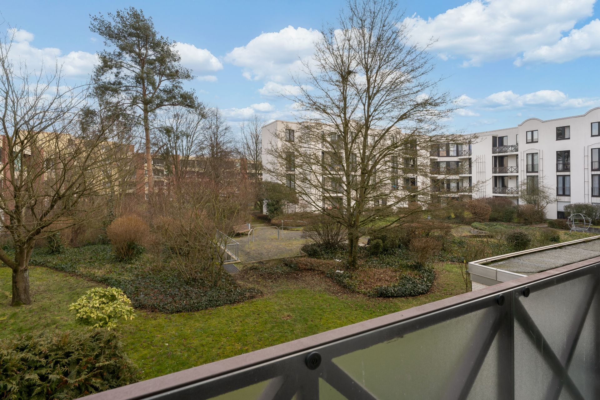 Blick vom Balkon auf einen begrünten Innenhof mit Bäumen und modernen Wohngebäuden.