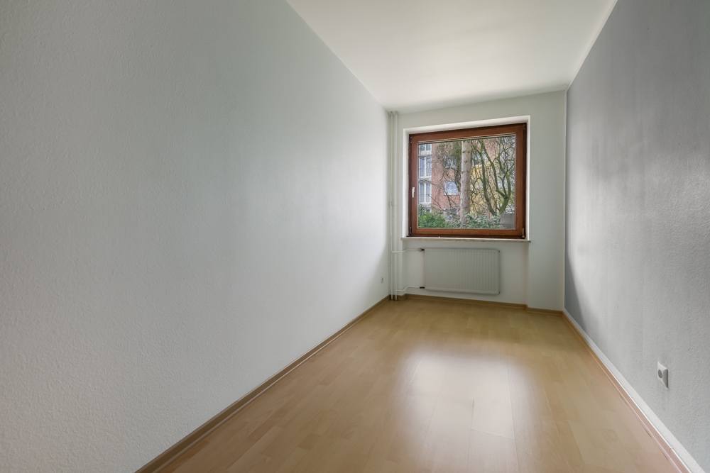 Leerer, schmaler Raum mit hellem Holzboden und großem Fenster an der Stirnseite.