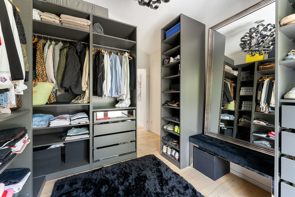Begehbarer Kleiderschrank mit offenen Regalen, Hängestangen, großem Spiegel und schwarzem Teppich.