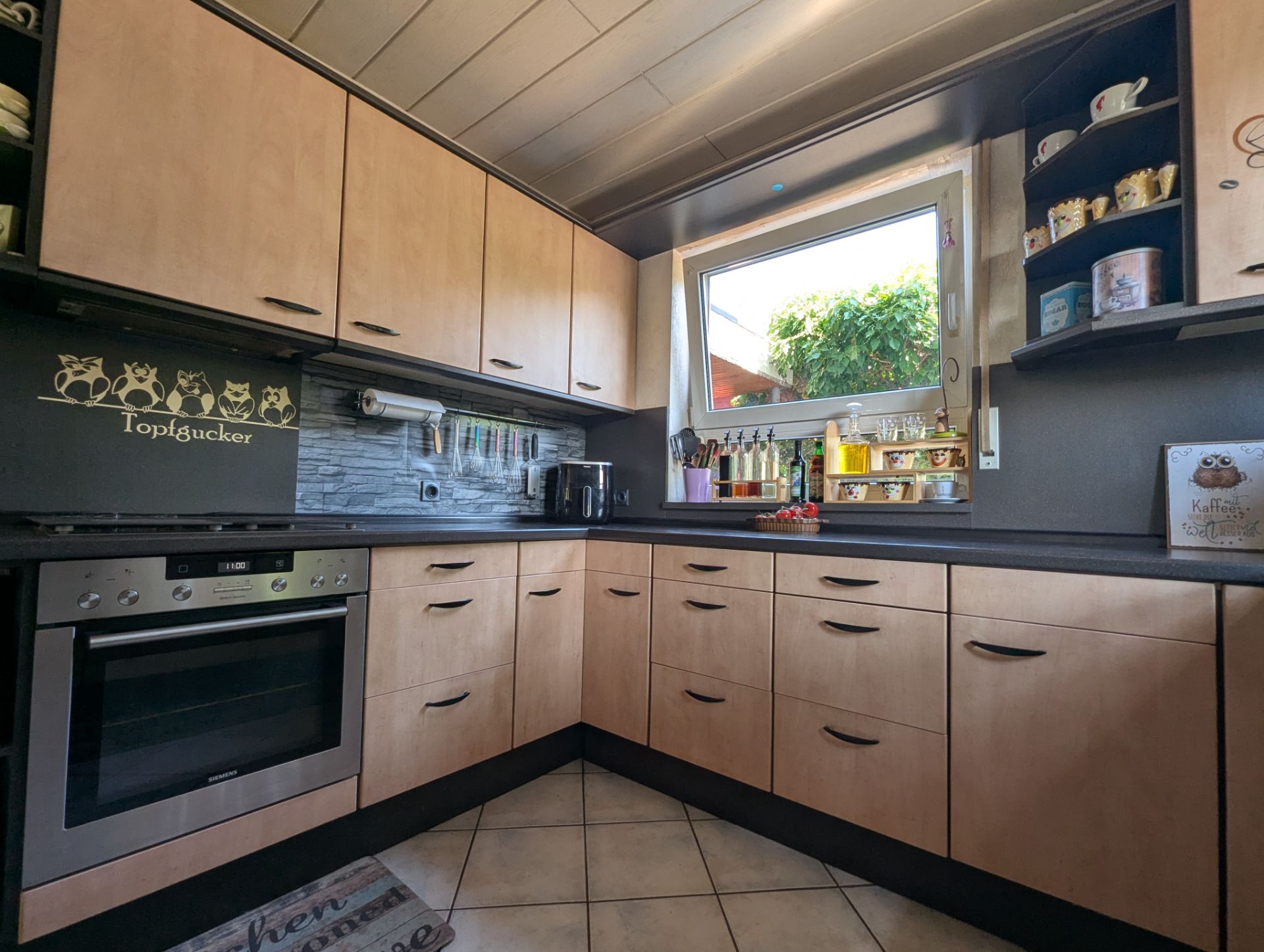 Moderne Küche mit Holzschränken, Herd, großem Fenster und verschiedenen Küchenutensilien.