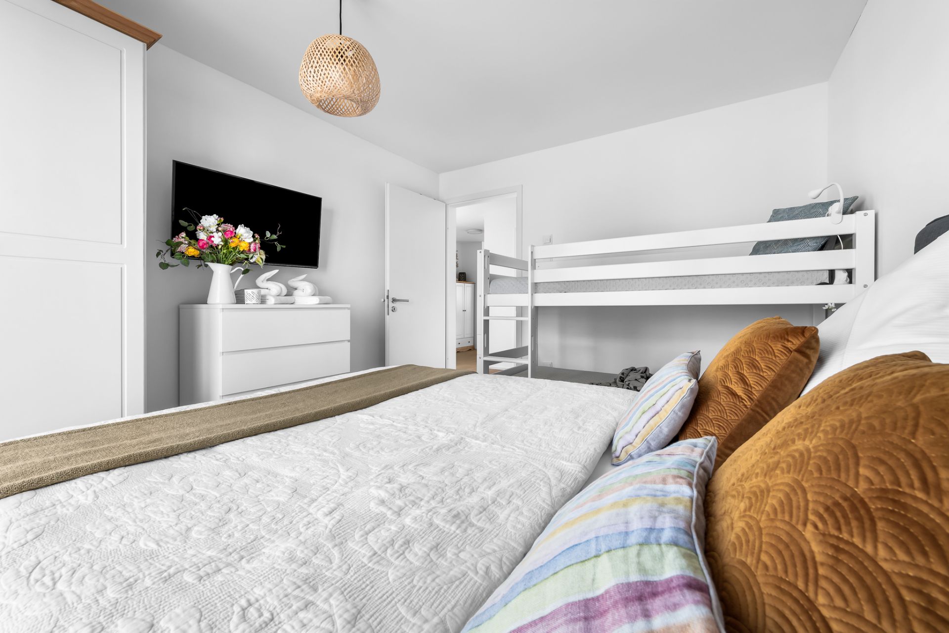 Schlafzimmer mit Doppelbett, Etagenbett, Kommode, Fernseher und offenen Tür.