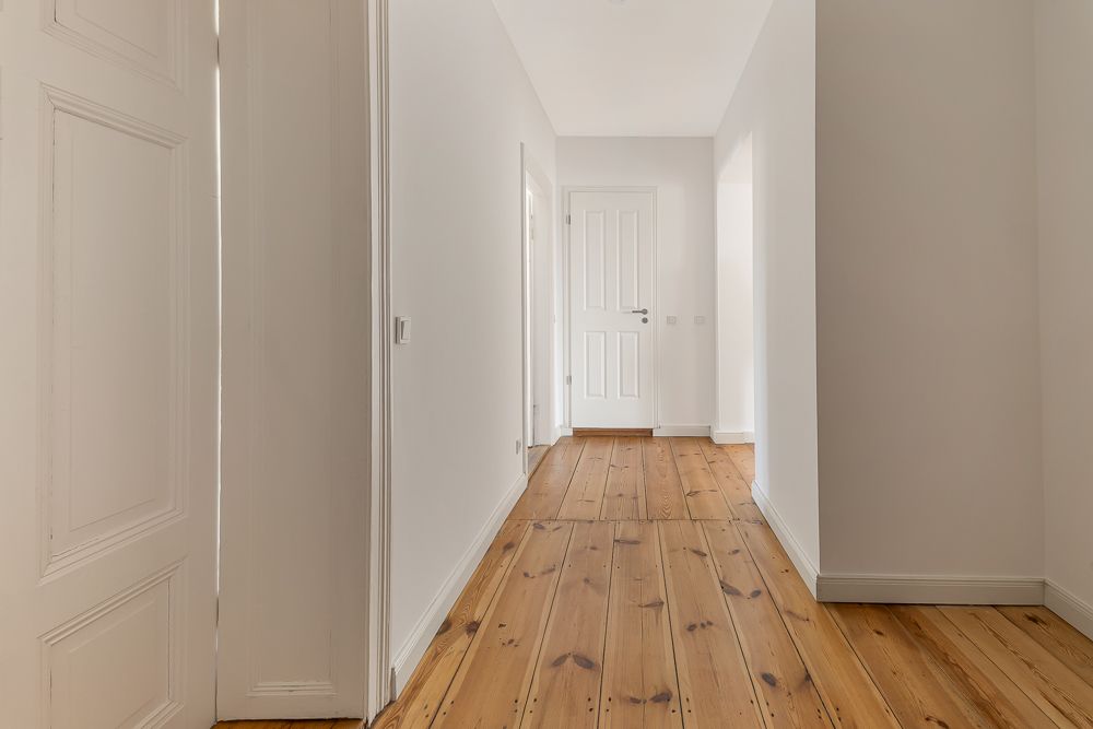 Heller Flur mit Holzboden und weißen Wänden, Türen führen in andere Zimmer.