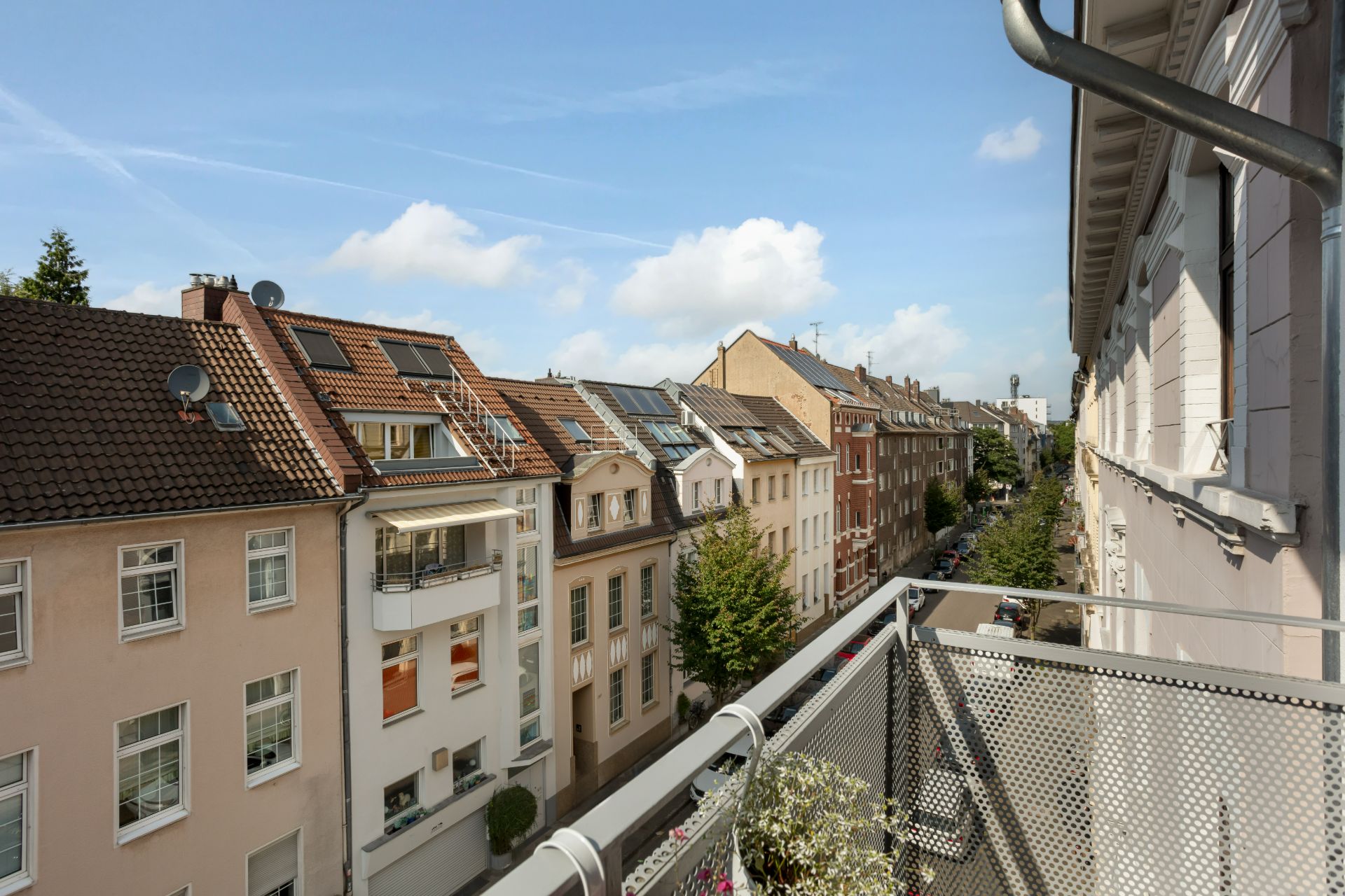Blick von einem Balkon auf eine Wohnstraße mit Mehrfamilienhäusern und Bäumen.