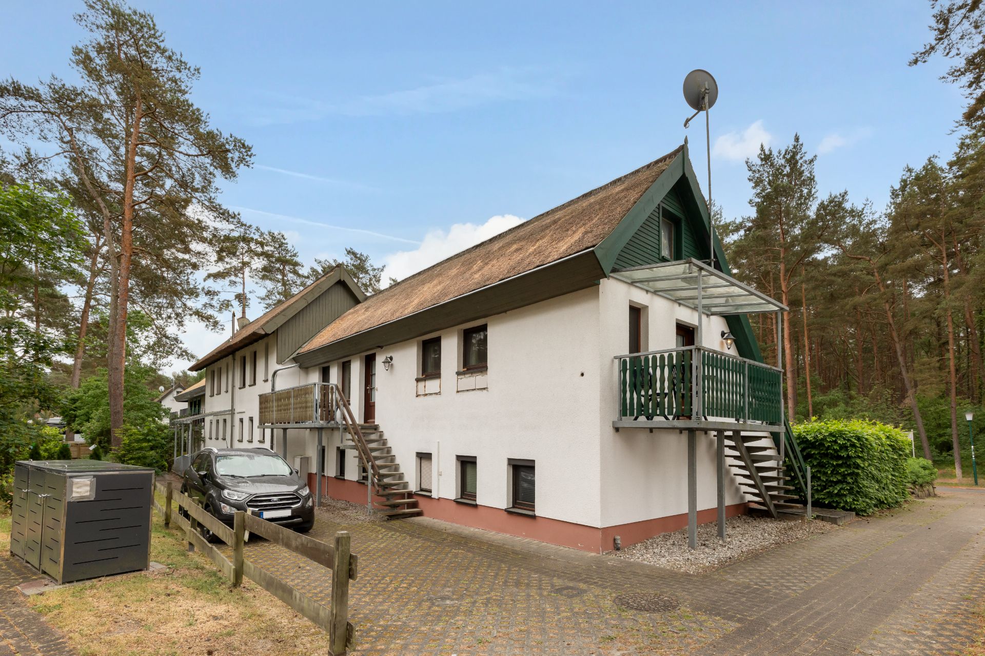Zweistöckiges Wohnhaus mit Außentreppen, Balkon und umgeben von Bäumen.