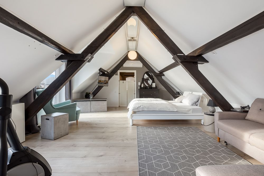 Geräumiges Dachgeschosszimmer mit sichtbaren Holzbalken, Bett, Sofa und Sessel.