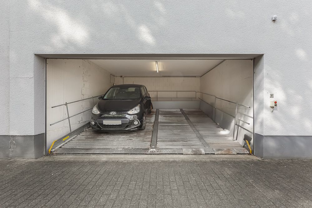 Ein schwarzes Auto parkt in einer offenen Garage mit weiß gestrichenen Wänden.