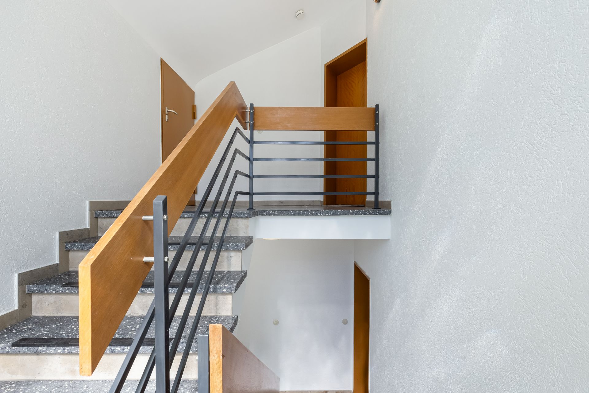 Treppenhaus mit grauen Stufen, weißen Wänden und Holztüren in einem Wohngebäude.