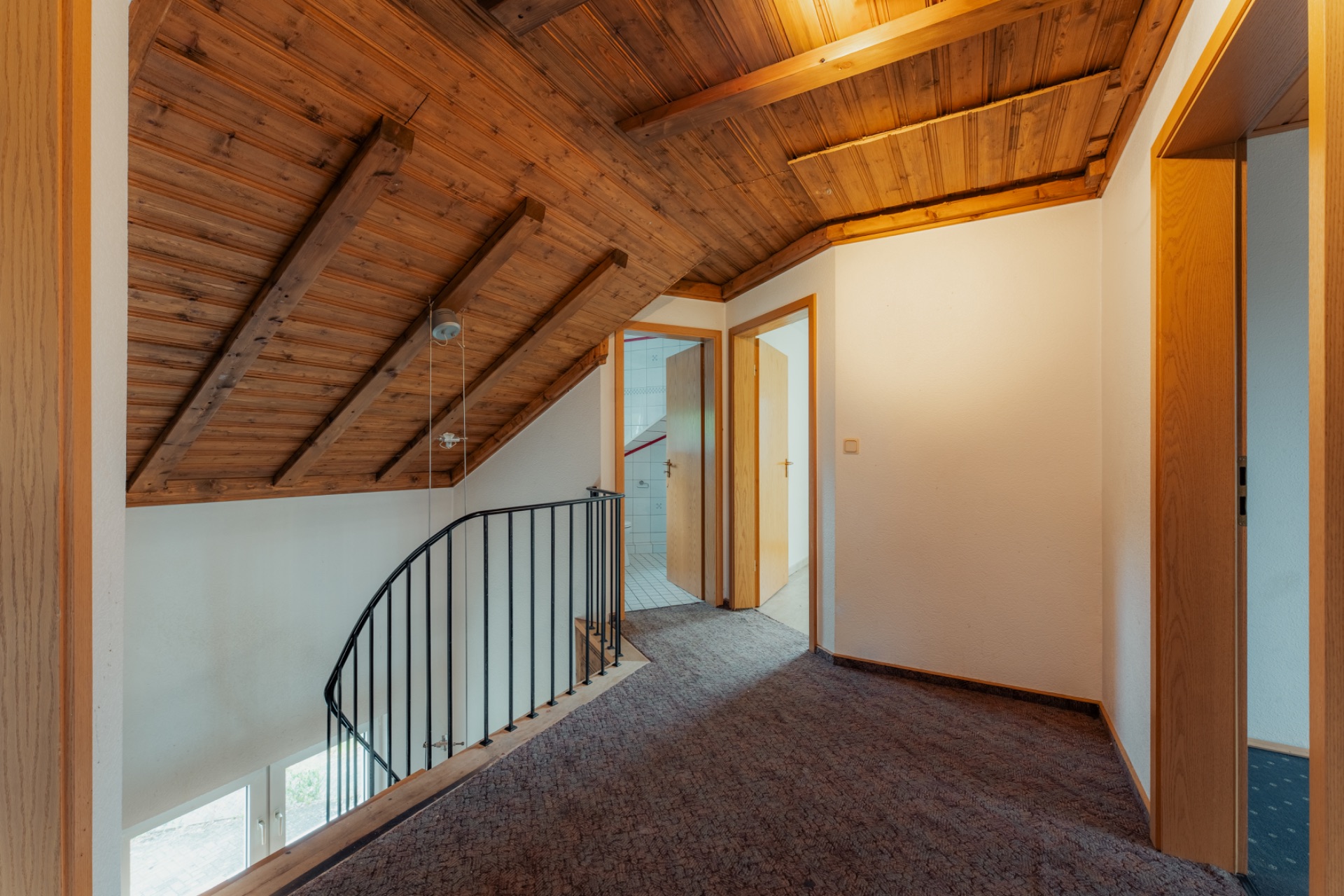 Flur eines Hauses mit schräger Holzdecke, Teppichboden und Treppengeländer.