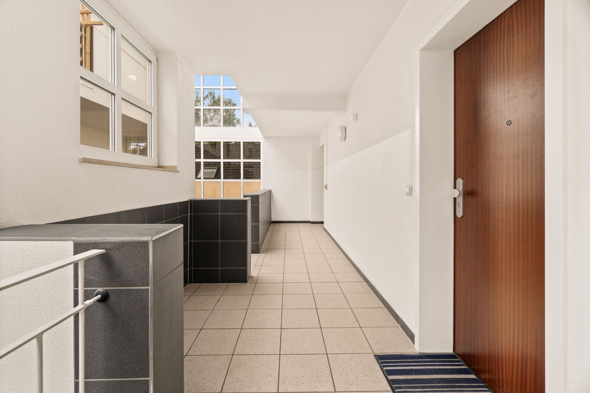 Heller Flur in einem Wohnhaus mit Fliesenboden und Holztür.