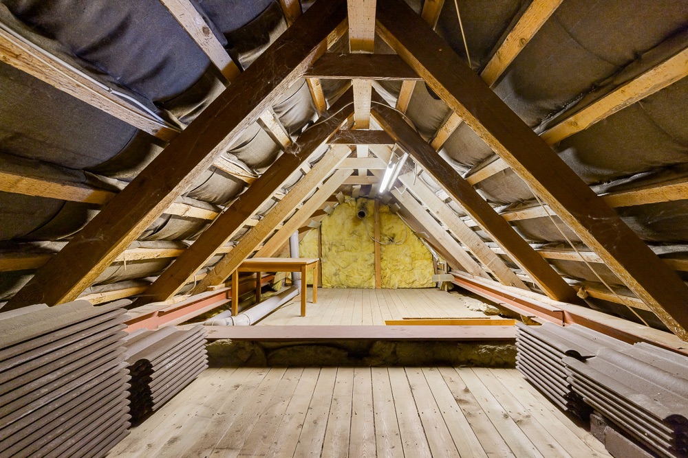 Ausgebauter Dachboden mit sichtbaren Holzbalken und einem Tisch an der Rückwand.