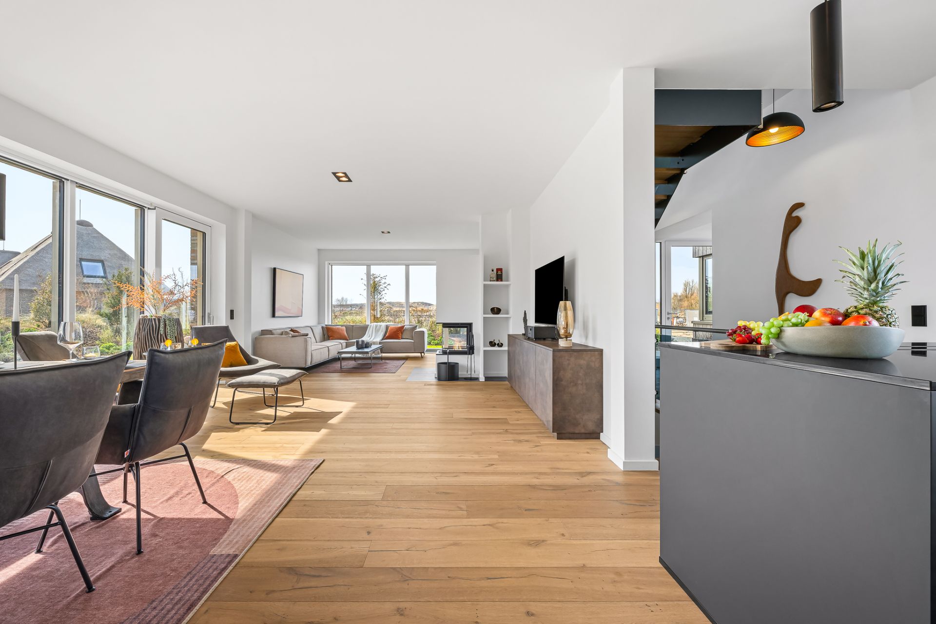 Helles Wohnzimmer mit Holzfußboden, Essbereich, Sofa und großen Fenstern.